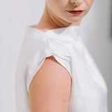 White Drape High Neck Top by Lika Designs, showcasing its flowing fabric and elegant high neckline on a consignment clothing hanger.
