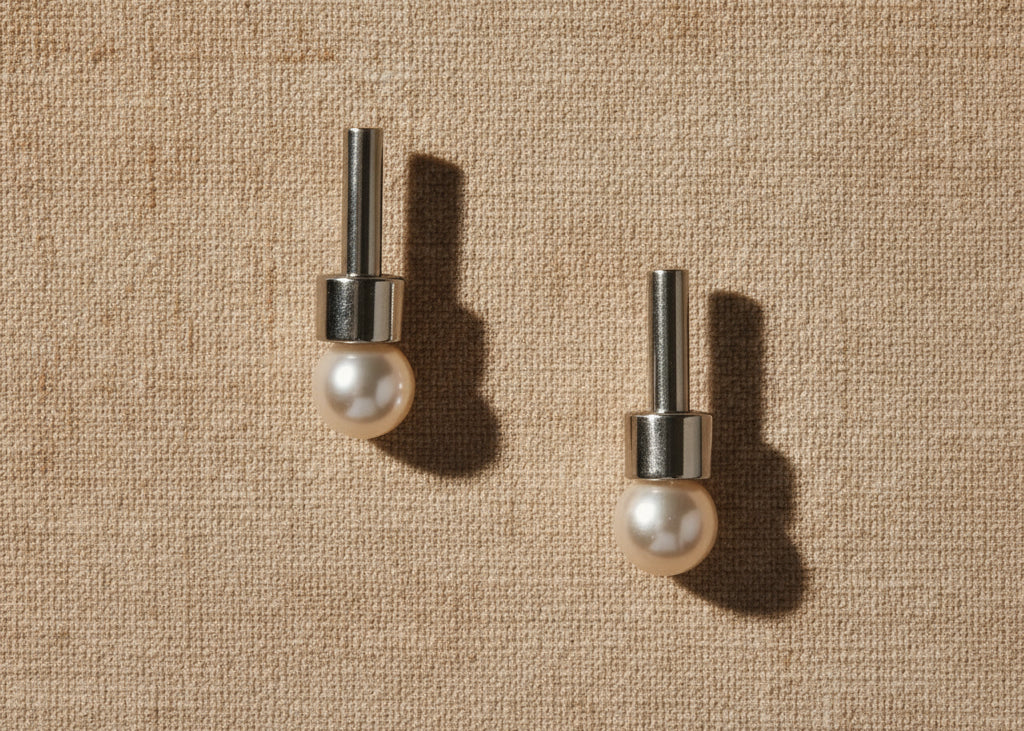 A pair of silver-colored earrings with a straight, round, metallic rod and an 8mm round white cultured pearl at the bottom.